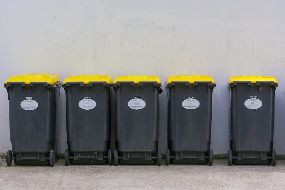A black wheeled refuse bin positioned on the edge of a paved street at night, marked with the label 'St. John's', filled with various types of waste such as cardboard, plastic containers, and paper. T